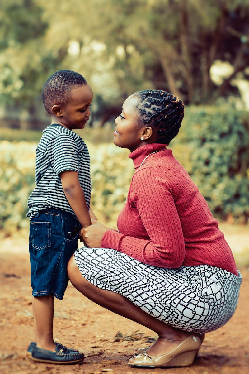 Tilt Shift Lens Photography of Woman Wearing Red Sweater and White Skirt While Holding a Boy Wearing White and Black Crew-neck Shirt and Blue Denim Short